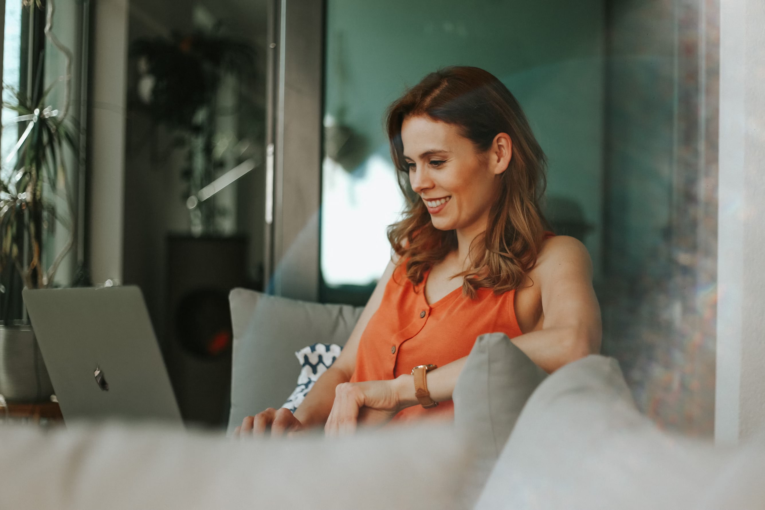 A smiling woman sitting on a couch using a laptop computer.